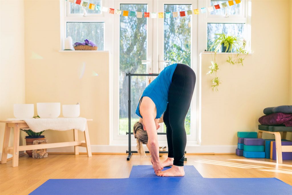 Varvara demonstrating Uttanasana – Forward Fold, in her Lymington Yoga Studio