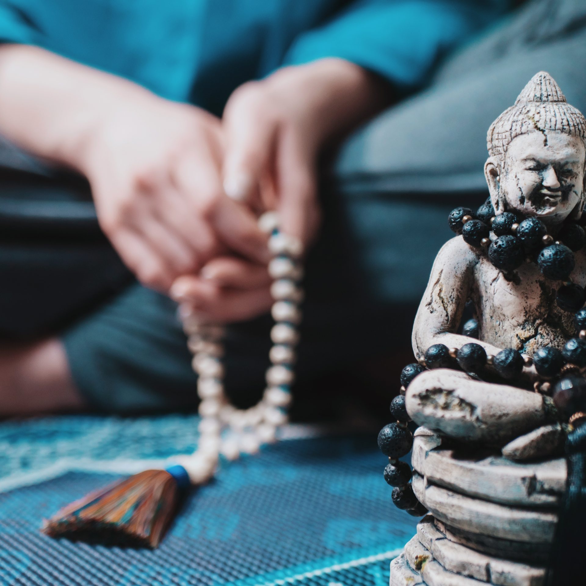 Concentrated woman praying with wooden rosary mala beads. Namaste. Close up statue of Buddha.